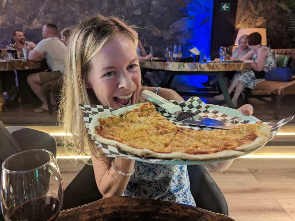 Penny holding up a large cheese pizza my her mouth