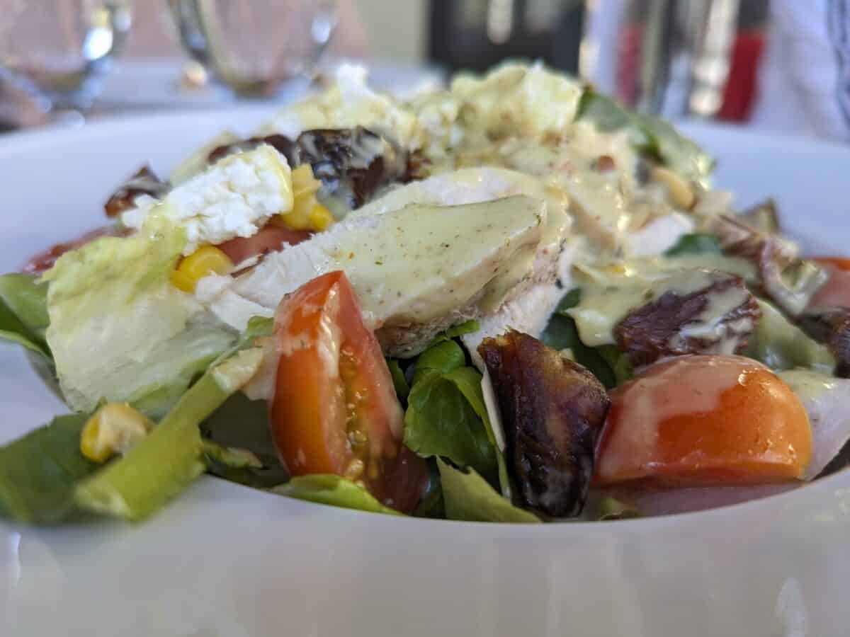 French Country Chicken Salad—an exquisite medley of flavors featuring roasted chicken, romaine, arugula, avocado, Campari tomatoes, grilled corn, Sphinx dates, local goat cheese, toasted almonds, and a tarragon-mustard vinaigrette