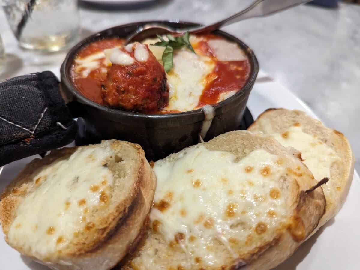 Bowl of cheesy meatballs and bread with cheese on a platter
