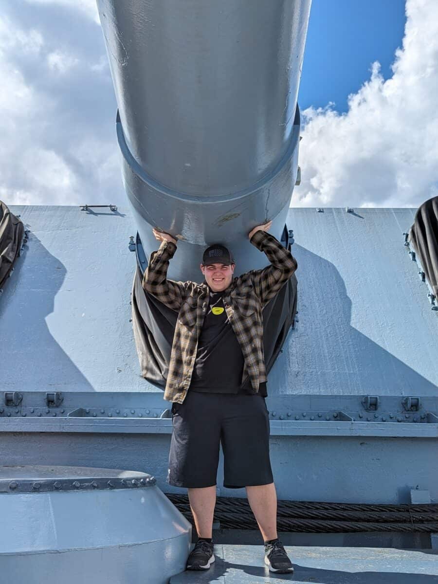 Tyler standing under naval gun holding both sides with his hands